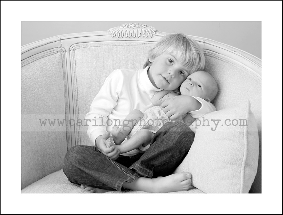 This image shows a proud big brother holding his new baby brother.  The image of the newborn baby boy by photographer Cari Long.